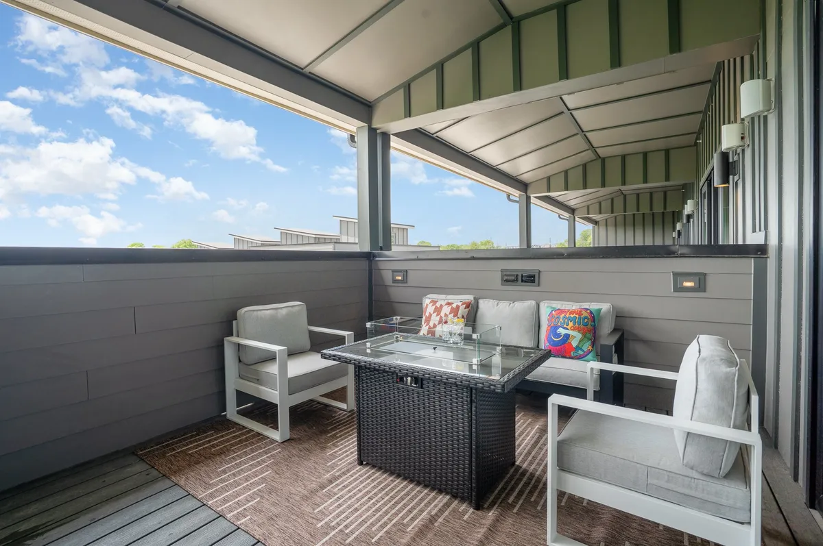 A tranquil outdoor seating arrangement with a glass-top table and decorative cushions, set against a serene backdrop. The space invites socializing, relaxation, and informal group conversations, perfect for after-work wind-downs or casual breakout sessions.