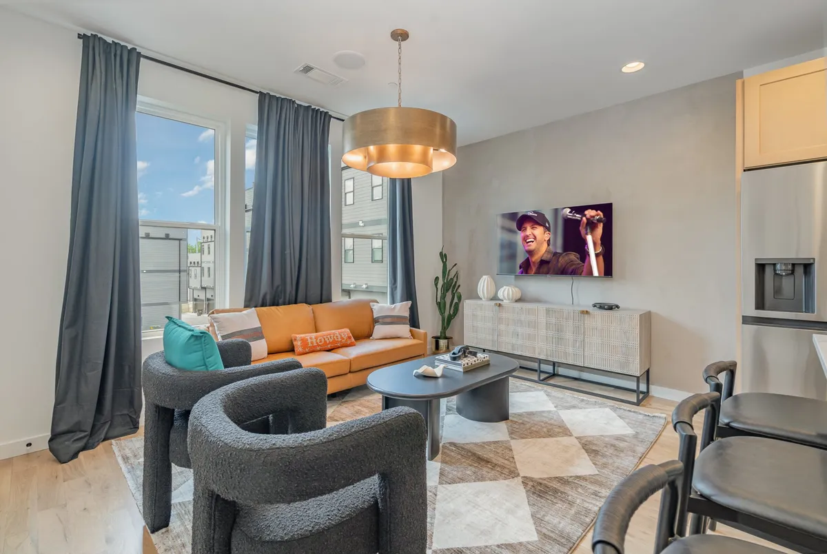 A stylish, country-chic living area with a bold orange sofa and black chairs arranged around a decorative rug. The TV displays a live music performance, creating a lively and cozy atmosphere perfect for socializing. The setup invites groups to relax, entertain, and enjoy quality time together.