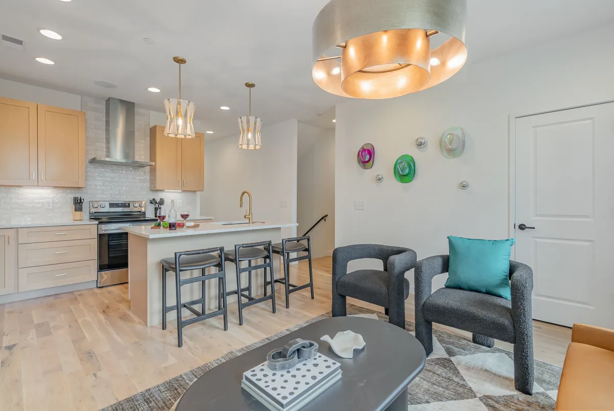 A contemporary kitchen with a spacious island, modern hanging light fixtures, and comfortable bar seating. Artwork on the wall and an adjacent seating arrangement hint at a seamless connection to the living or dining area, ideal for hosting and casual dining.