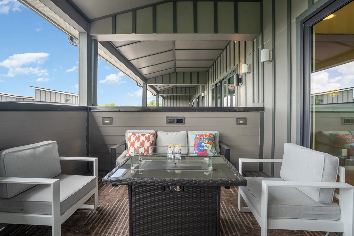 A stylish rooftop terrace with outdoor seating, a glass table with refreshments, and decorative cushions, set against a backdrop of the evening sky. The cozy, inviting space is perfect for relaxing, socializing, and stargazing after a night out.