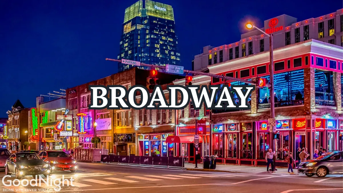 A bustling nighttime streetscape filled with neon signs, people walking, cars, and illuminated buildings along Nashville's lively Broadway area. The scene captures the energetic spirit of the city's renowned nightlife and music scene.