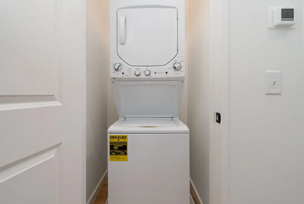 This image depicts a clean, compact laundry space with a stacked washer and dryer next to pristine white walls and open doorways, conveying a sense of practicality and freshness.