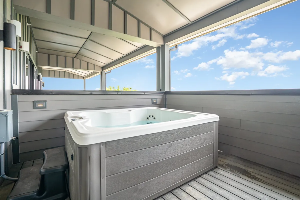 A rooftop wooden deck with a hot tub overlooking the Nashville skyline. The open sky above sets the mood for stargazing or enjoying a soak with friends, capturing the essence of an outdoor urban retreat.